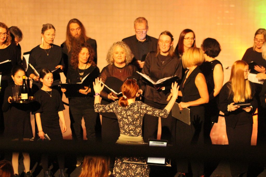 Eine Sängerin aus dem Jugendchor der Chorakademie Wolfsburg steht vor dem Kammerchor und dirigiert.