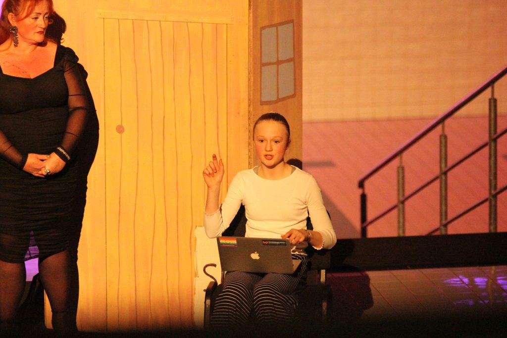 Eine Schauspielerin des Jugendchor Cantiamo Chorakademie Wolfsburg sitzt mit einem Laptop auf der Bühne und muss Geschäftliches regeln